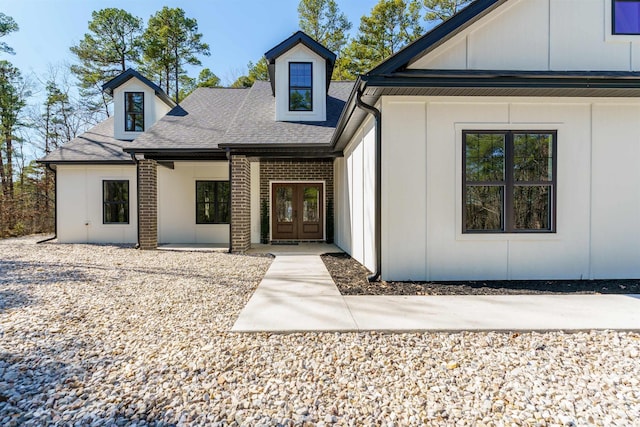 view of front of property featuring board and batten siding, a shingled roof, french doors, and brick siding