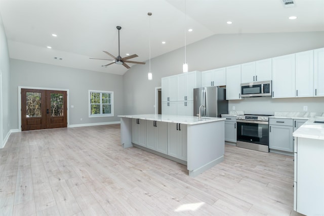 kitchen with light wood finished floors, open floor plan, a kitchen island with sink, stainless steel appliances, and light countertops