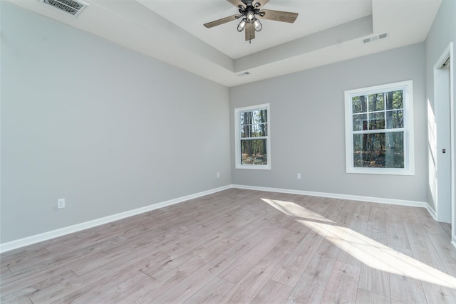 spare room with light wood-style flooring, visible vents, a raised ceiling, and baseboards