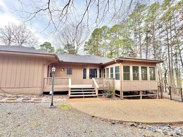 view of front of house with a deck, fence, roof with shingles, a sunroom, and a chimney