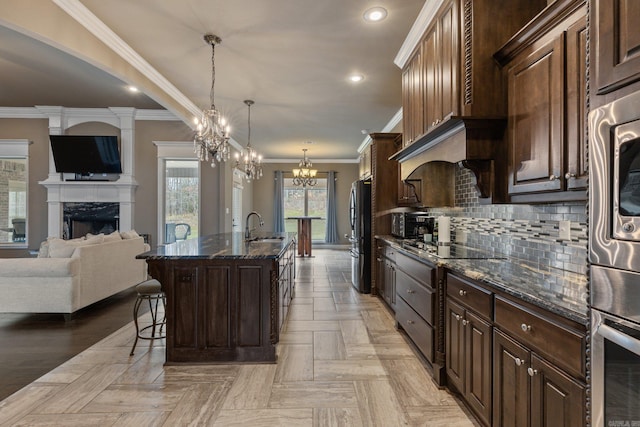 kitchen with dark stone counters, a premium fireplace, black appliances, a kitchen bar, and a sink