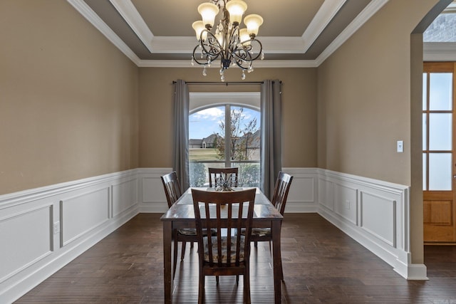 dining area with arched walkways, a tray ceiling, dark wood-style flooring, and a notable chandelier