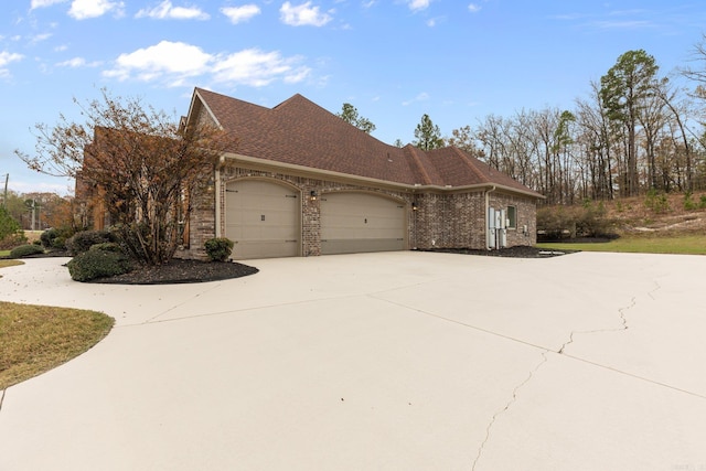 view of home's exterior featuring a shingled roof, concrete driveway, brick siding, and an attached garage