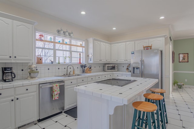 kitchen featuring a sink, tile counters, appliances with stainless steel finishes, and a breakfast bar area