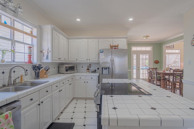 kitchen featuring a sink, appliances with stainless steel finishes, tile counters, and ornamental molding