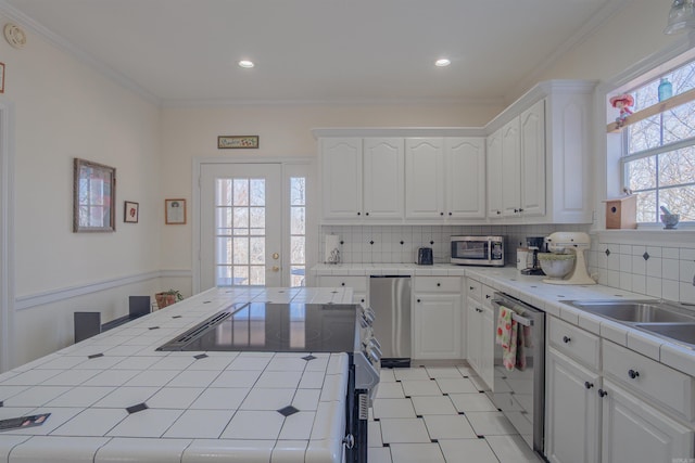 kitchen featuring tile countertops, appliances with stainless steel finishes, white cabinetry, and crown molding