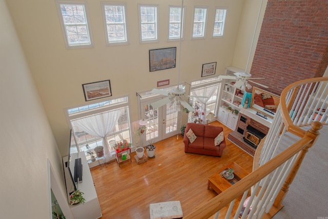 living area featuring a towering ceiling, brick wall, ceiling fan, wood finished floors, and a fireplace