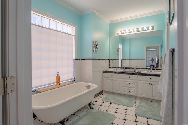 full bath with a sink, tile walls, a freestanding bath, double vanity, and crown molding