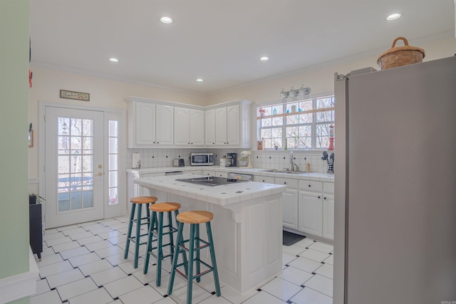 kitchen with tile countertops, a breakfast bar area, stainless steel appliances, white cabinetry, and a sink