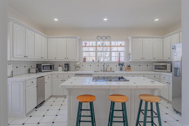 kitchen featuring tile countertops, a breakfast bar area, stainless steel appliances, and a sink