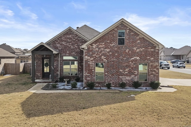 view of front of property featuring brick siding, a front lawn, and fence