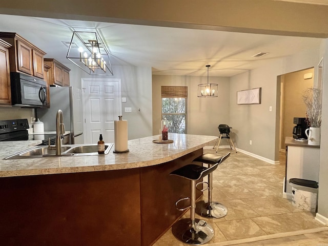 kitchen featuring visible vents, a peninsula, black appliances, a kitchen bar, and a sink