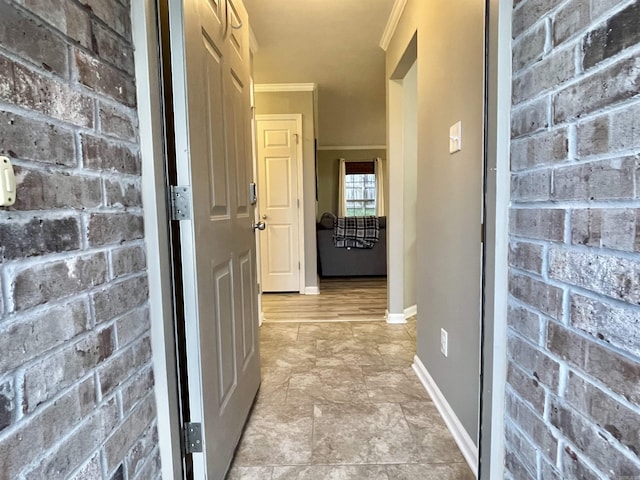 hallway with brick wall, baseboards, and crown molding