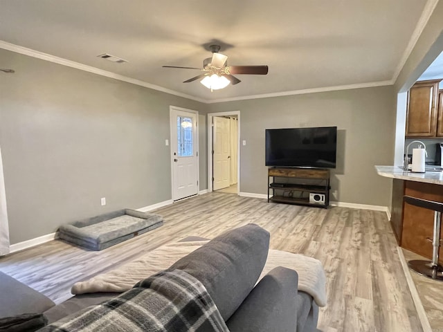 living room featuring ornamental molding, light wood-type flooring, visible vents, and baseboards