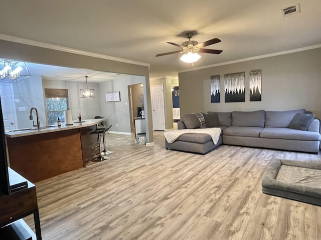 living area with ceiling fan with notable chandelier, visible vents, baseboards, light wood-type flooring, and crown molding