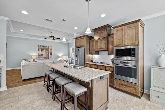 kitchen featuring decorative backsplash, a breakfast bar area, appliances with stainless steel finishes, crown molding, and a sink