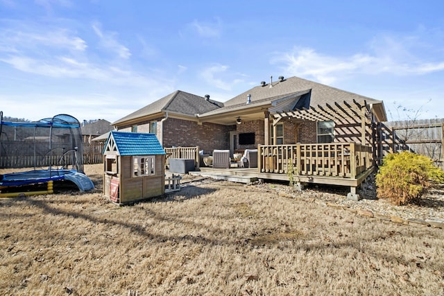 rear view of house with a trampoline, brick siding, fence, and a wooden deck