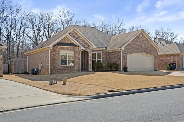 view of front facade featuring central AC unit, an attached garage, brick siding, a shingled roof, and driveway