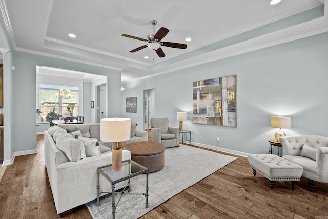 living room with baseboards, ornamental molding, a raised ceiling, and wood finished floors