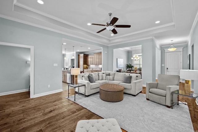 living room featuring recessed lighting, wood finished floors, baseboards, a tray ceiling, and crown molding