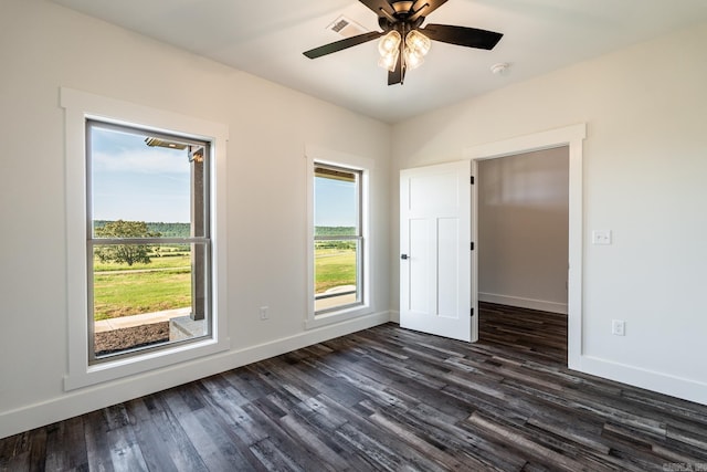 empty room with dark wood-style flooring, visible vents, and baseboards