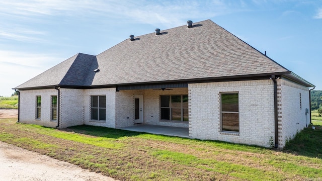 rear view of property with brick siding, roof with shingles, a lawn, a patio area, and ceiling fan