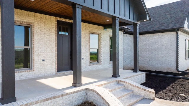 view of exterior entry featuring brick siding and roof with shingles