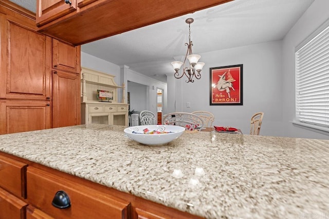 kitchen featuring a chandelier, pendant lighting, brown cabinets, and light stone countertops