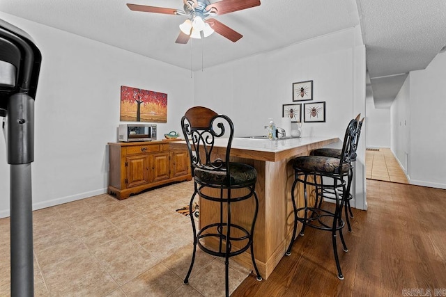 kitchen featuring a peninsula, a ceiling fan, a kitchen breakfast bar, light countertops, and stainless steel microwave