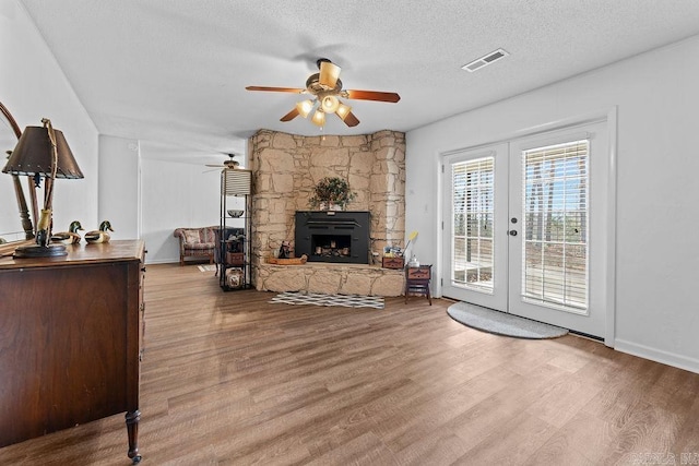 living area with visible vents, wood finished floors, a textured ceiling, french doors, and a fireplace