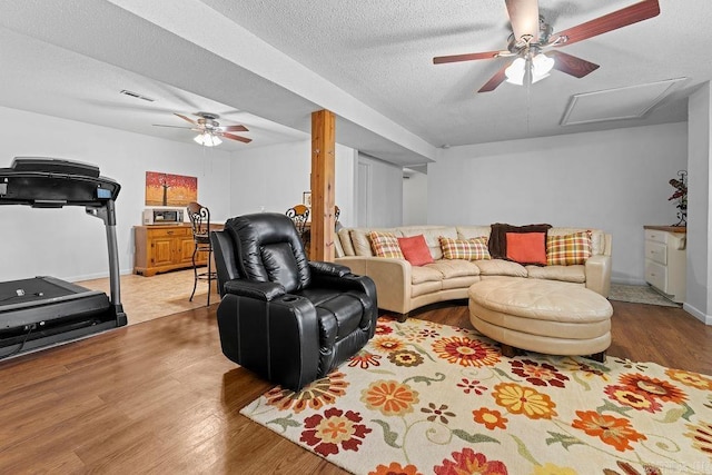 living area with a textured ceiling, ceiling fan, wood finished floors, and visible vents