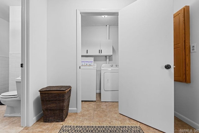 washroom with light tile patterned floors, washing machine and clothes dryer, cabinet space, and baseboards