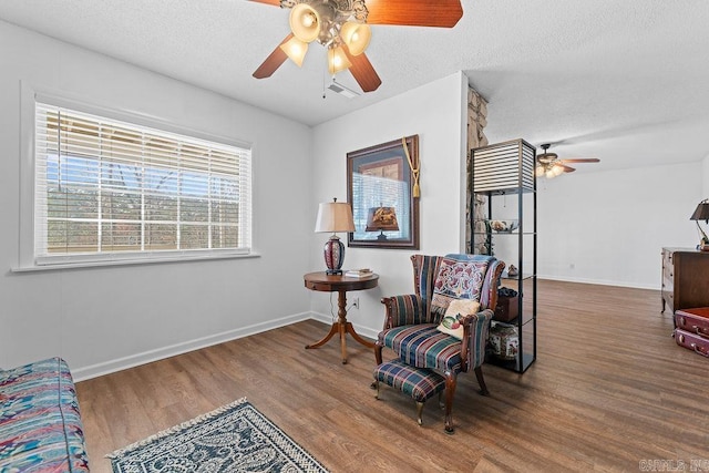 living area featuring visible vents, a textured ceiling, baseboards, and wood finished floors