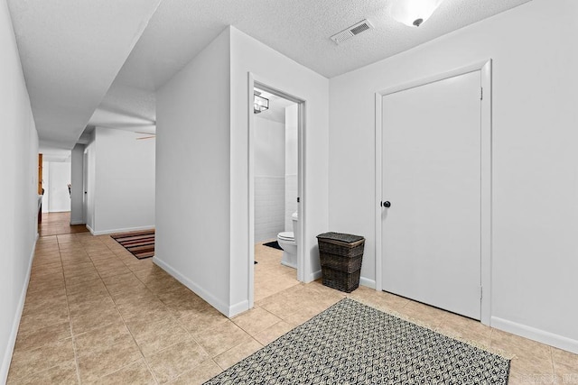 hall featuring visible vents, a textured ceiling, baseboards, and light tile patterned flooring