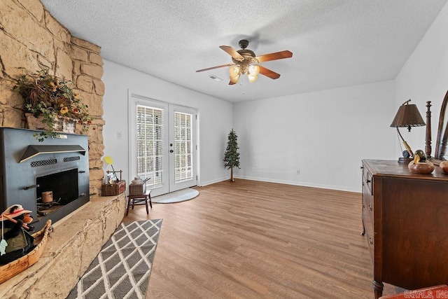 sitting room featuring baseboards, french doors, wood finished floors, a textured ceiling, and a stone fireplace