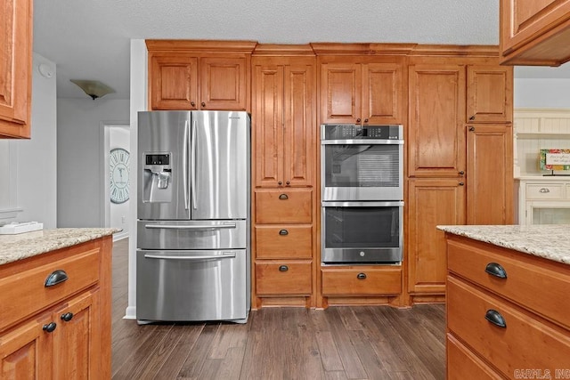 kitchen with stainless steel appliances, brown cabinets, light stone counters, and dark wood-style floors