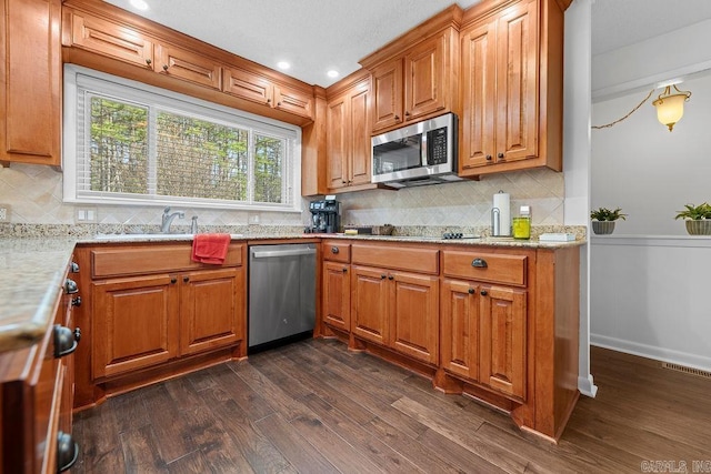 kitchen featuring appliances with stainless steel finishes, dark wood-type flooring, a sink, and brown cabinetry