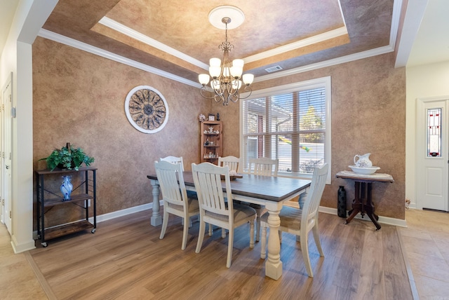 dining room featuring crown molding, an inviting chandelier, a raised ceiling, and light wood-style floors