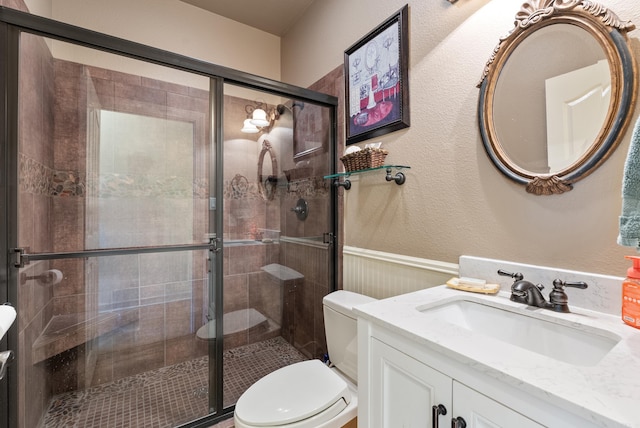 bathroom featuring a textured wall, vanity, a shower stall, and toilet