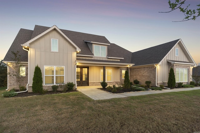 view of front of home with board and batten siding, french doors, brick siding, and a yard