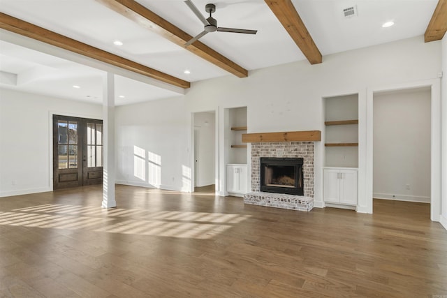 unfurnished living room featuring beam ceiling, visible vents, a brick fireplace, wood finished floors, and baseboards