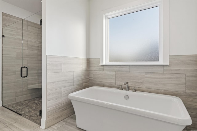 bathroom featuring a stall shower, a freestanding bath, and tile walls