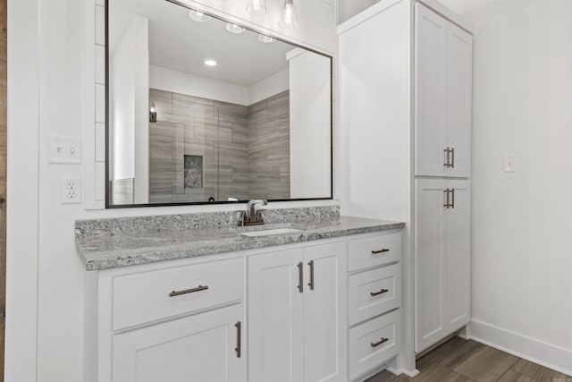 bathroom featuring wood finished floors, a tile shower, vanity, and baseboards