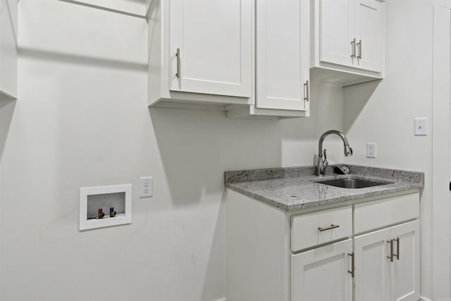 kitchen featuring light stone counters, a sink, and white cabinets