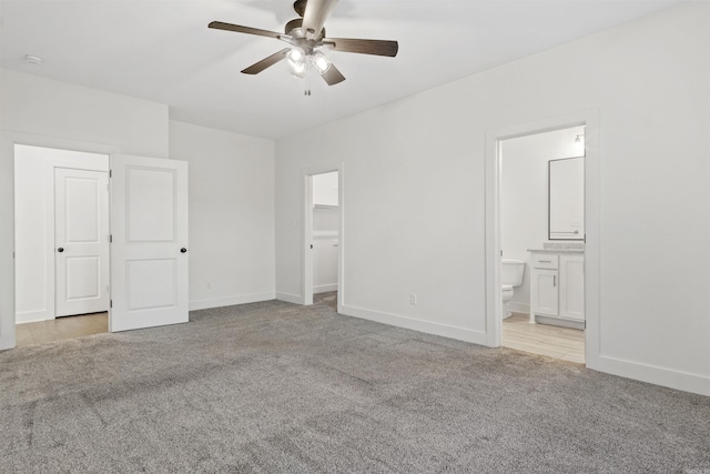 unfurnished bedroom featuring carpet, a walk in closet, ensuite bathroom, ceiling fan, and baseboards