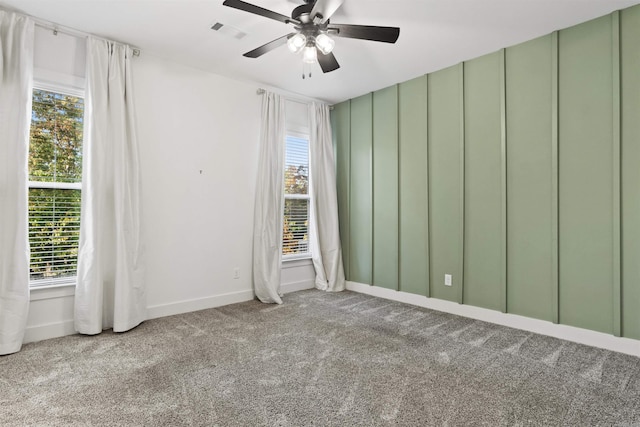 carpeted empty room with ceiling fan, a decorative wall, visible vents, and baseboards