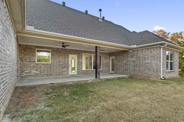 back of house with brick siding, roof with shingles, a patio area, and a lawn