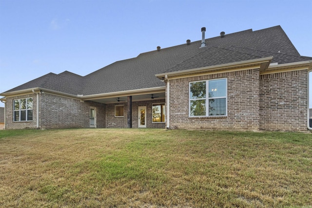 back of property featuring ceiling fan, a yard, a shingled roof, and brick siding