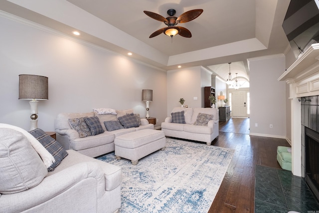 living area featuring ornamental molding, a tray ceiling, dark wood-style flooring, and a tile fireplace