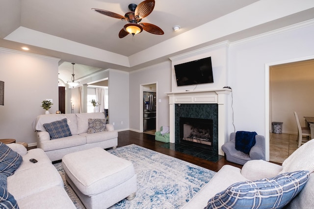 living room with dark wood-style floors, a raised ceiling, a premium fireplace, ornamental molding, and ceiling fan